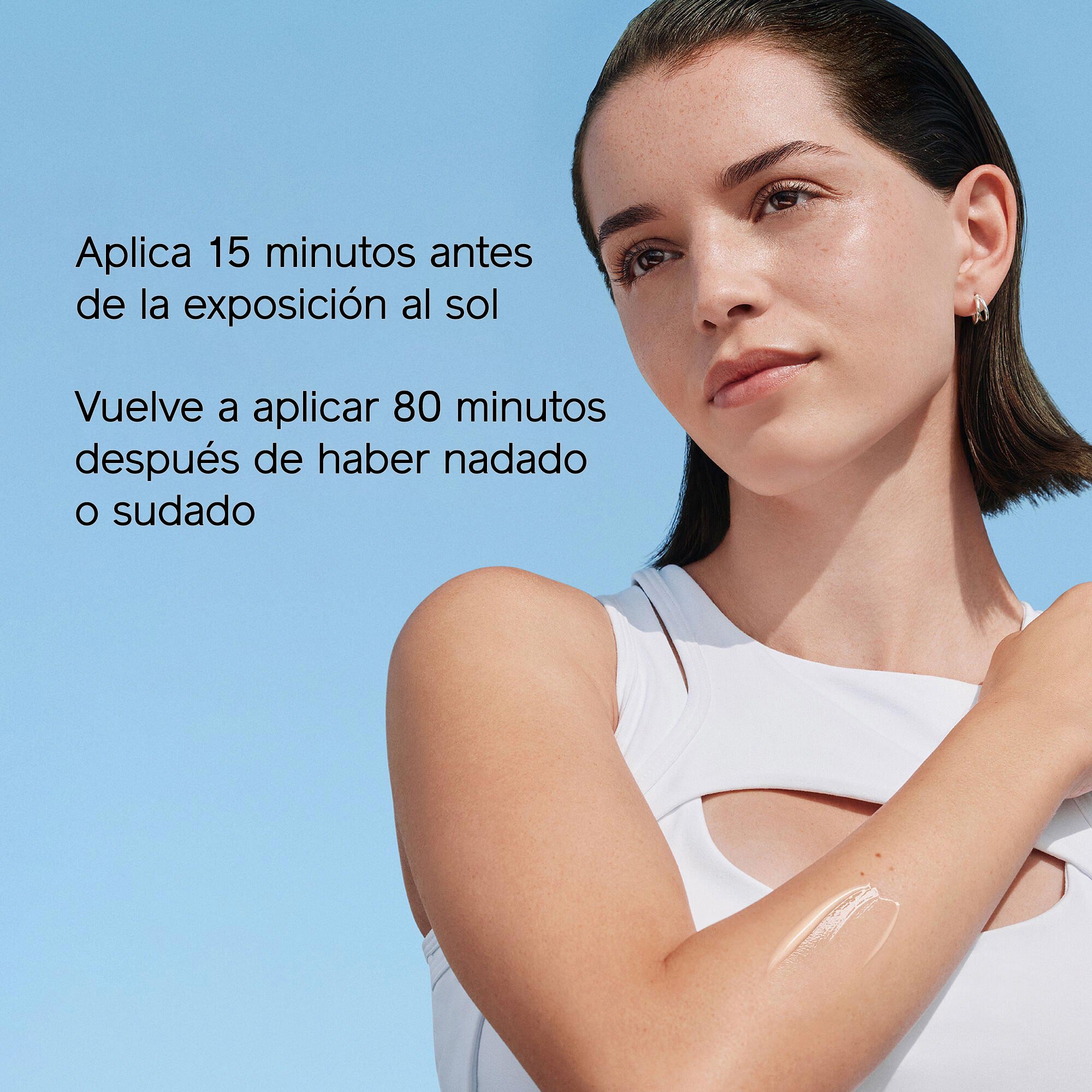 Una mujer exhibe la muestra de un producto de tratamiento en el brazo con un fondo de cielo azul. En el texto de la izquierda se lee: "Aplica 15 minutos antes de la exposición al sol" y "Vuelve a aplicar después de 80 minutos de haber nadado o sudado".
